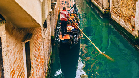 A traditional gondola navigates a vibrant green canal in Venice, flanked by aged, textured buildings, offering a classic Italian experience.の写真素材