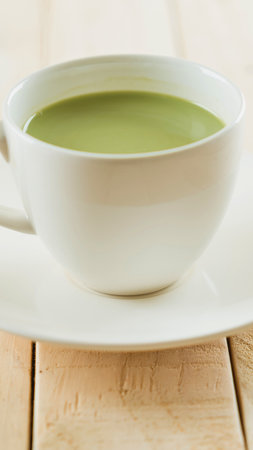 A steaming cup of vibrant green matcha tea sits on a white saucer, ready to be enjoyed on a wooden surface.の写真素材