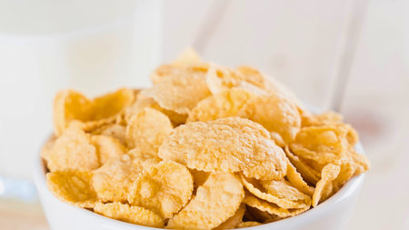 A close-up shot of a white bowl overflowing with crunchy, golden corn flakes, ready for breakfast.