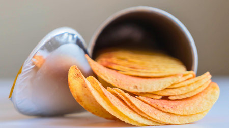 Thinly sliced, golden potato chips are artfully arranged and spilling from an overturned metal bowl, creating a tempting snack display.の写真素材