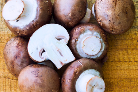 A close-up overhead view of several whole and halved cremini mushrooms arranged on a textured wooden background.の写真素材