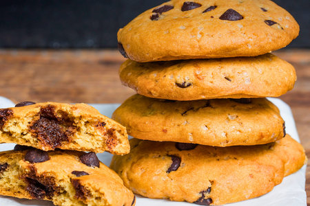 A close-up shot of a stack of freshly baked chocolate chip cookies, with one cookie broken in half...