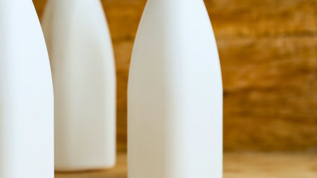 A close-up shot focuses on three white bottles with smooth surfaces, arranged in a row against a warm, textured backdrop.の写真素材