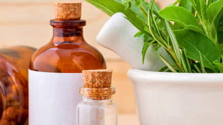 A mortar and pestle filled with fresh herbs sits beside amber glass bottles containing herbal remedies and essential oils.の写真素材
