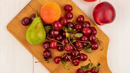 A vibrant overhead view of a wooden cutting board filled with a colorful assortment of fresh fruits including cherries pears apricots and plums.の写真素材