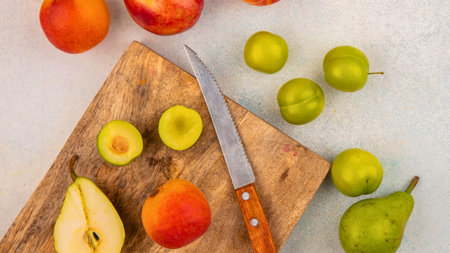 A variety of fresh fruits including pears, plums, and apricots are arranged on and around a rustic wooden cutting board with a knife.の写真素材
