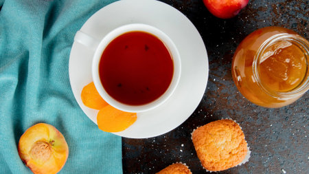 A warm cup of tea, a jar of jam, fresh fruit, and a pastry create a delightful breakfast or afternoon treat.の写真素材