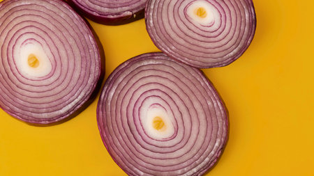 Several cross-sections of red onions are arranged on a bright yellow surface, showcasing their concentric rings and purple outer layers.の写真素材