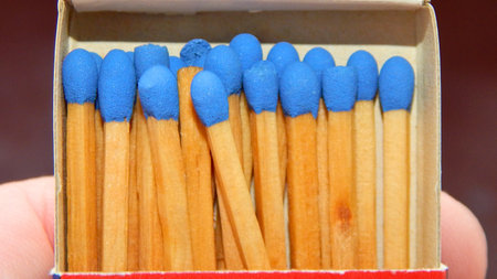 A close-up view of a box filled with wooden safety matches, each tipped with vibrant blue.の写真素材