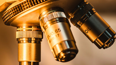 Detailed view of three metallic microscope objective lenses, showcasing intricate design and a warm, golden hue.の写真素材