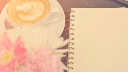 A soft focus image of a steaming cup of coffee, a blank notebook, and a delicate pink flower, evoking a peaceful morning.の写真素材