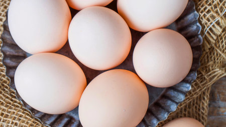 A close-up overhead view of several light brown eggs nestled in a rustic burlap-lined basket, suggesting freshness and natural origin.の写真素材