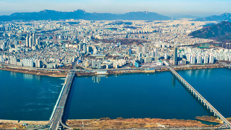 An expansive urban landscape unfolds beneath a clear sky, bisected by a large river spanned by two prominent bridges.の写真素材