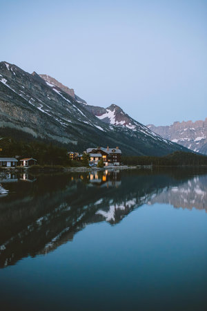 A peaceful mountain lake scene with houses, mountains, and a clear sky.