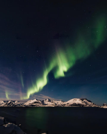 Bright northern lights illuminate the dark sky above snowy mountain peaks.