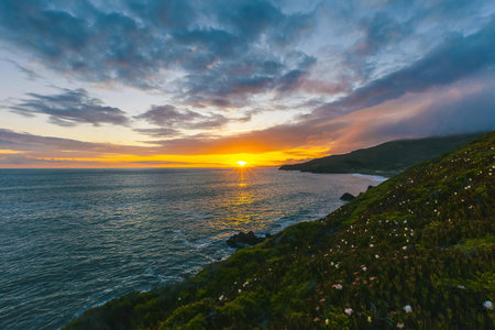 A vibrant sunset scene with colorful sky, ocean waves, and rocky coast