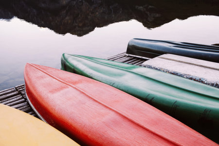 Bright kayaks in green, blue, and yellow on a dock near water and mountains