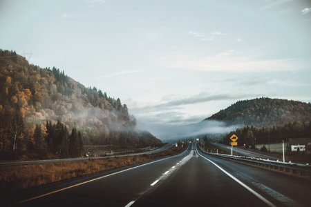 A quiet highway stretches through mountains under a cloudy sky, peaceful scene