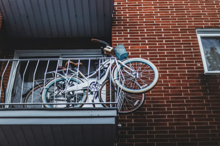 A bicycle with a water bottle hangs on a balcony railing against a colorful brick wall in an urban setting.