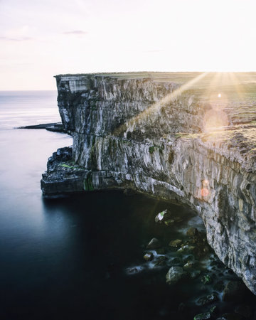 A scenic view of a rocky cliff overlooking the ocean during sunset with vibrant colors.