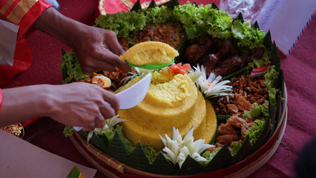 Chef serving nasi tumpeng (cone rice) served with urap-urap (Indonesian salad), fried chicken and noodles. Nasi tumpeng is usually served at birthday parties or Thanksgivingの写真素材
