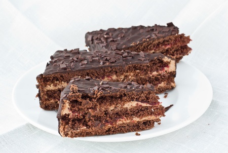 3 pieces of chocolate cake with cherry jam lying on white plate with white linen background の写真素材