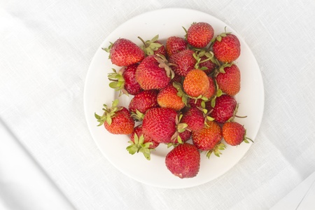 Strawberries lying in a form of triangle on a white plate with background made of linen tableclothの写真素材