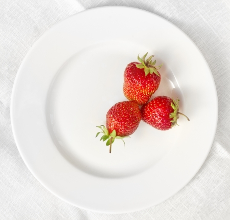 3 strawberries lying in a form of triangle on a white plate with background made of linen tableclothの写真素材