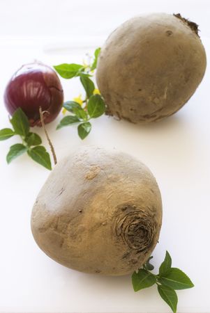 Beetroot and onion with green leafs on white cutting boardの写真素材