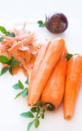 Peeled carrots and onion with green leafs on white cutting boardの写真素材