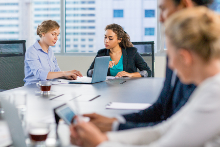 Young business people sitting in modern office, working on laptop and tablet computerの写真素材