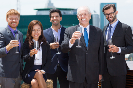 Group of five smiling business people standing on rooftop of office building, holding glasses with champagne and celebrating business success. Business team conceptの写真素材