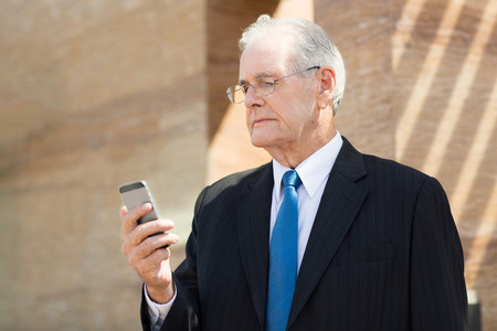 Portrait of mature businessman standing outdoors and looking at smartphoneの写真素材