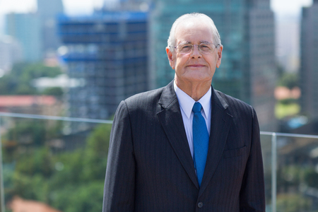 Portrait of senior businessman standing on rooftop of office building, smiling, looking at cameraの写真素材