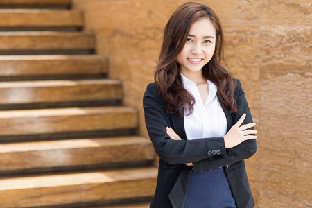 Portrait of young Asian businesswoman standing with crossed arms outside office and smiling at cameraの写真素材