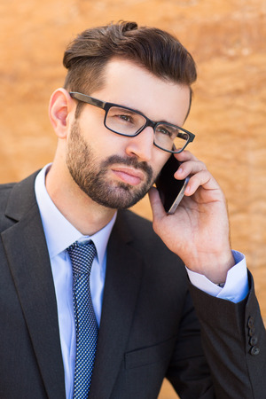 Portrait of serious young businessman wearing glasses talking on smartphoneの写真素材
