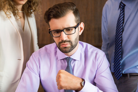 Close up portrait of confused businessman looking at something out of view and thinking with male and female colleagues seen partly in backgroundの写真素材