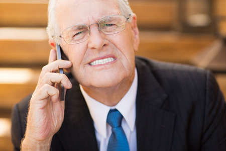 Close up portrait of worried senior businessman talking on mobile phone and clenching his teethの写真素材