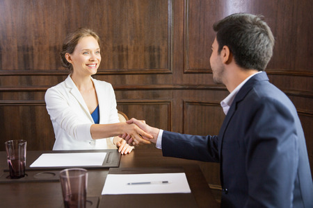 Portrait of young Caucasian businesswoman sitting in conference room and shaking hands with her male partner after finishing meetingの写真素材