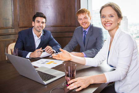 Group of three business people having meeting in conference room, cheerful businesswoman pointing to laptop screen and discussing business plan with male colleaguesの写真素材