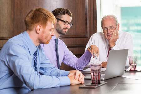 Business team sitting in conference room, looking at laptop screen and discussing business project. Teamwork conceptの写真素材