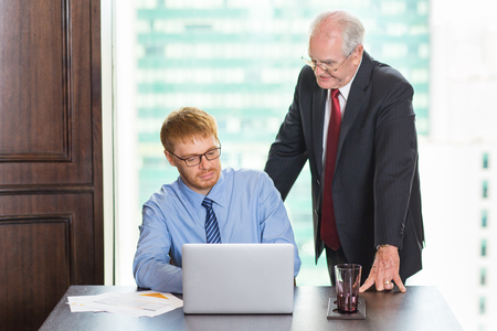 Two businessmen working on laptop in conference room. Senior businessman explaining important points of new business project to his young colleagueの写真素材