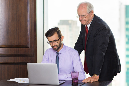 Senior businessman looking at laptop and checking work of his young colleagueの写真素材