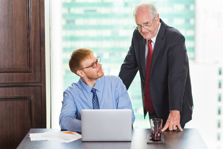 Senior businessman explaining business project idea. His young male colleague looking at him and listeningの写真素材