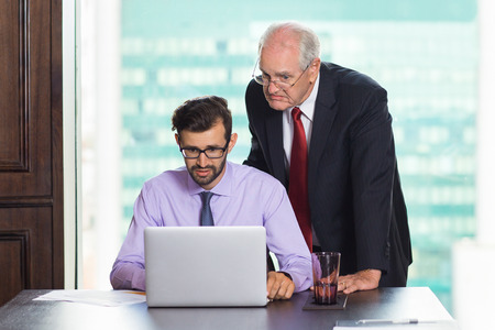 Two businessmen working on laptop in conference room. They are puzzled, checking report and trying to find mistakesの写真素材
