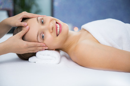 Happy young woman lying on back and getting head massage in spa center. She looking at camera and smilingの写真素材