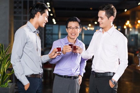 One senior and two young men smiling, toasting and standing in barの写真素材
