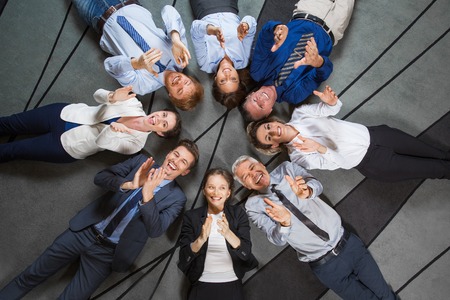 Eight smiling at camera business people lying on floor in circle and clapping. Top view.の写真素材