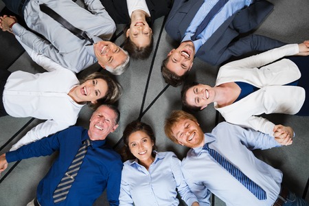 Closeup of eight smiling at camera business people lying on floor in circle and holding hands. Top view.の写真素材