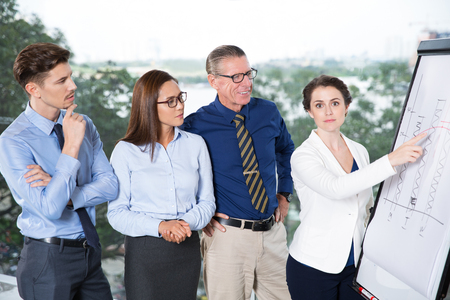Successful business team standing at presentation in office. Their female leader presenting bar chart on whiteboardの写真素材